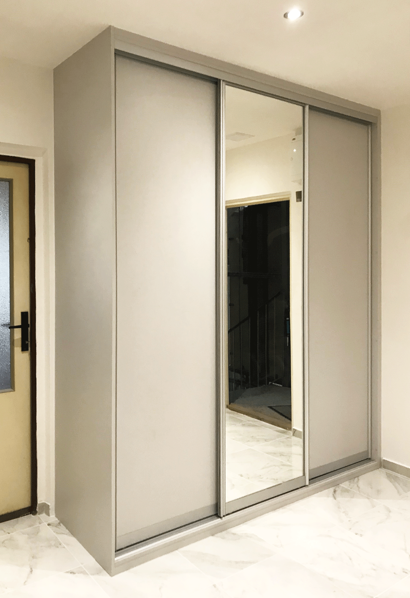 Vestavěná skříň s posuvnými dveřmi se zrcadlem ve světle šedivé barvě.