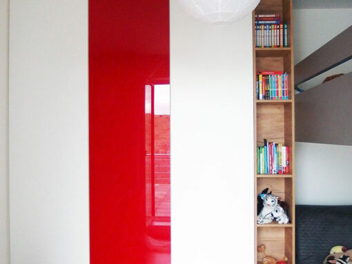 Vestavěná skříň s pantovými dveřmi v bílé barvě kombinovaná s červenými skleněnými dveřmi a dřevěnou otevřenou částí.
