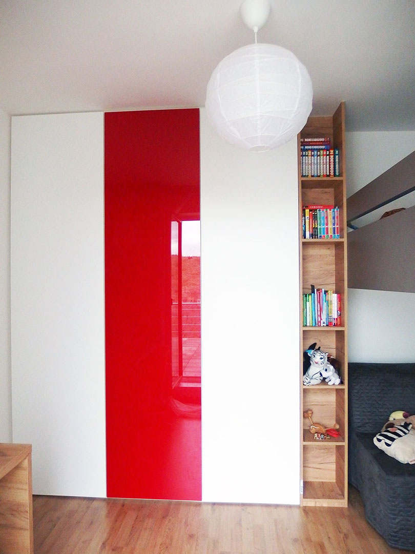 Vestavěná skříň s pantovými dveřmi v bílé barvě kombinovaná s červenými skleněnými dveřmi a dřevěnou otevřenou částí.