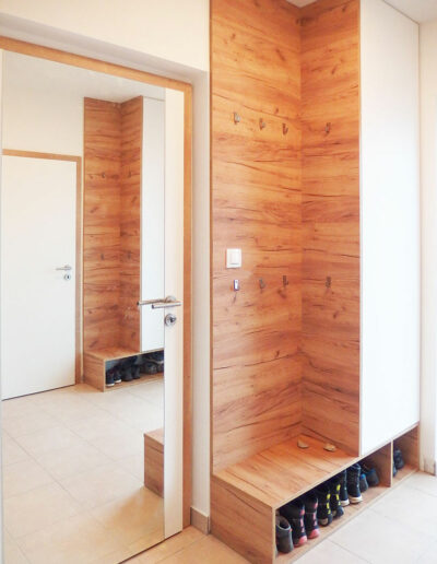 Skříň do chodby s věšáky v dubovém provedení s bílými pantovými dveřmi.