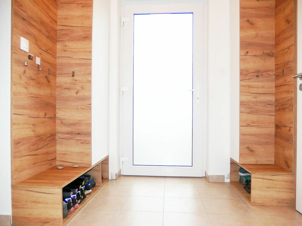 Vestavěné skříně do chodby s otevřeným botníkem v dubovém dekoru s bílými dveřmi.