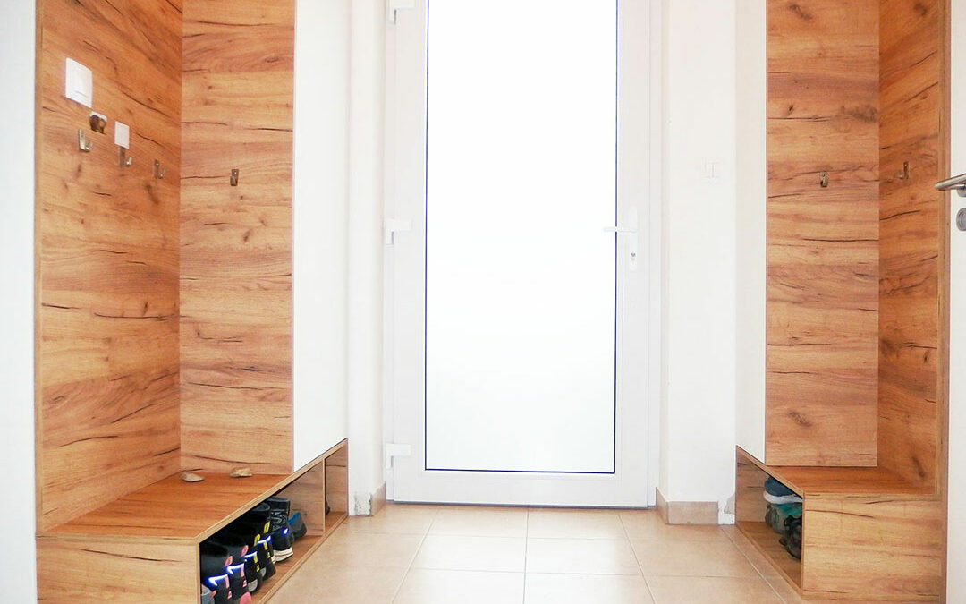 Vestavěné skříně do chodby s otevřeným botníkem v dubovém dekoru s bílými dveřmi.
