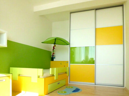 Dětský pokoj s postelí a vestavěnou skříní s posuvnými dveřmi.