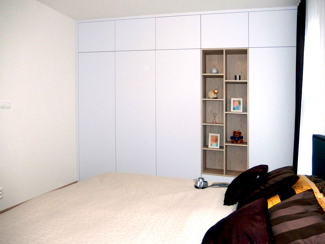 Vestavěná skříň do ložnice v bílé maté barvě s otevřenou dřevěnou částí.