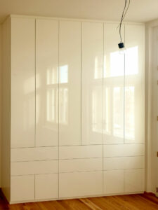 Realizace vestavěné skříně s pantovými dveřmi a šuplíky v bílém lesku.