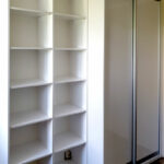 Realizace vestavěné skříně s posuvnými dveřmi a otevřenámi policemi v bílé barvě.