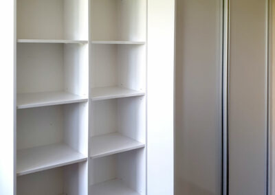 Realizace vestavěné skříně s posuvnými dveřmi a otevřenámi policemi v bílé barvě.
