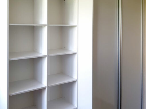 Realizace vestavěné skříně s posuvnými dveřmi a otevřenámi policemi v bílé barvě.