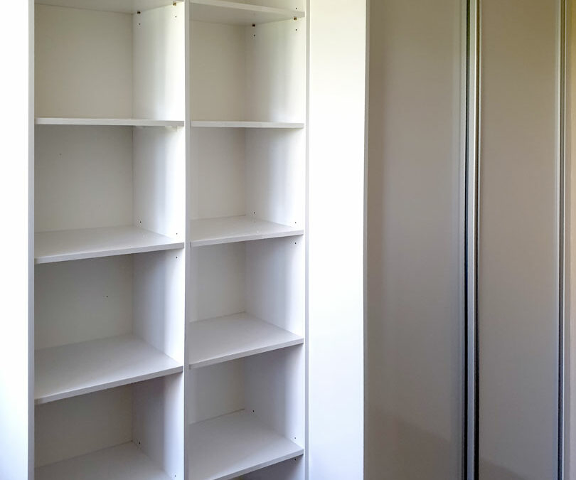 Realizace vestavěné skříně s posuvnými dveřmi a otevřenámi policemi v bílé barvě.