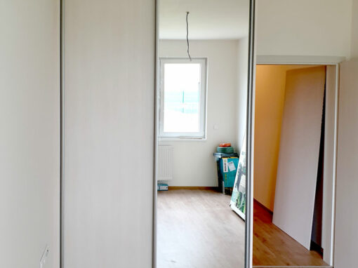 Realizace skříně na míru s posuvnými dveřmi. Kombinace světlého dřeba a zrcadla.