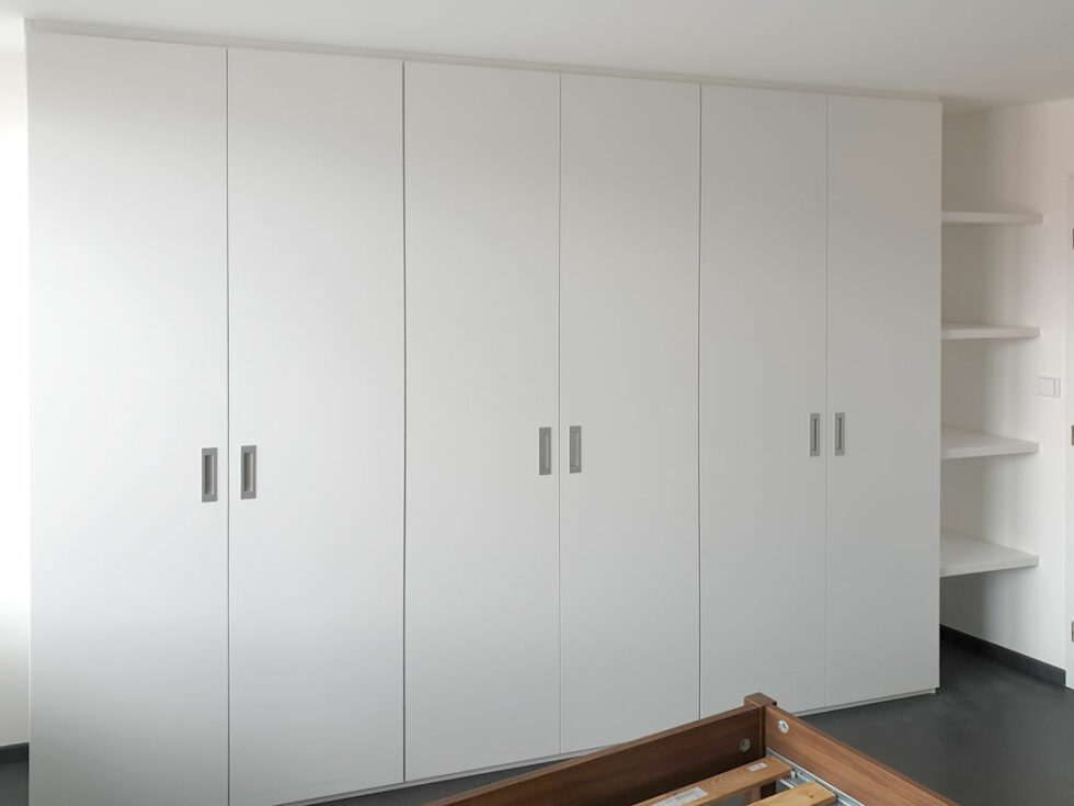 Realizace skříně na míru do ložnice s pantovými dveřmi v bílé barvě a zafrezovanými úchytkami.
