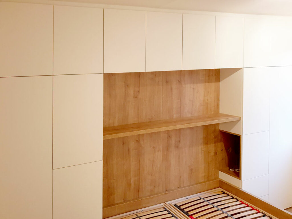 Obestavěná postel skříní s pantovými dveřmi.