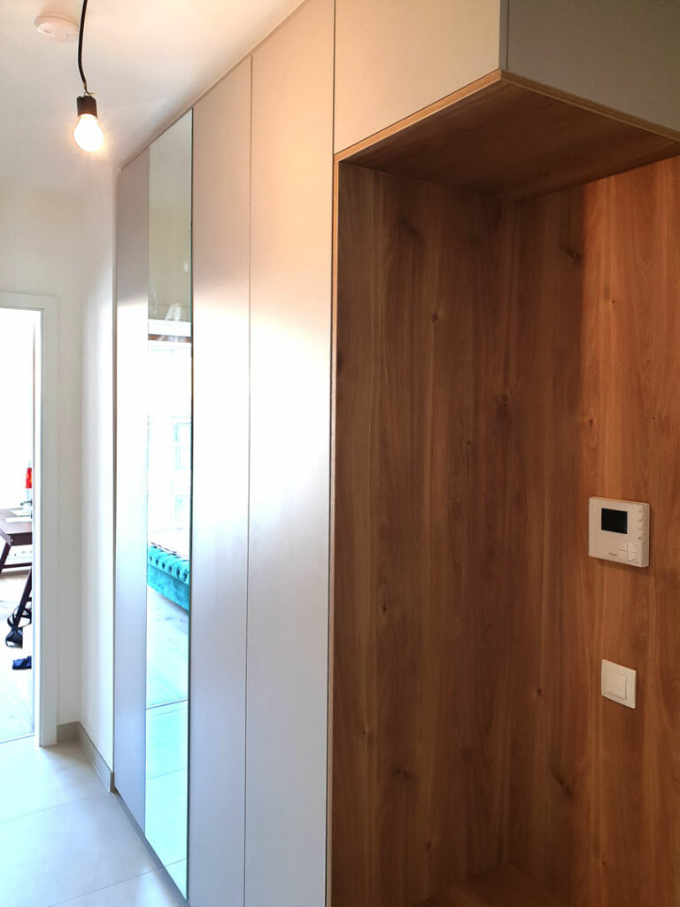 Realizace vestavěné skříňě do chodby s otevřenou dřevěnou částí a pantovými dveřmi.