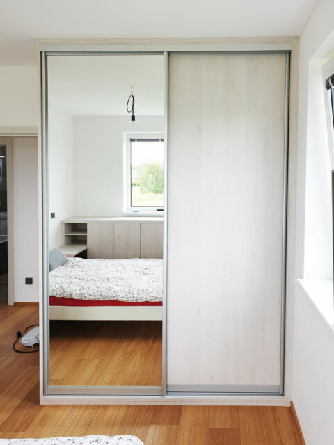 Realizace skříně na míru do ložnice s posuvnými dveřmi ve světlém dřevěném dekoru a zrcadlovými dveřmi.