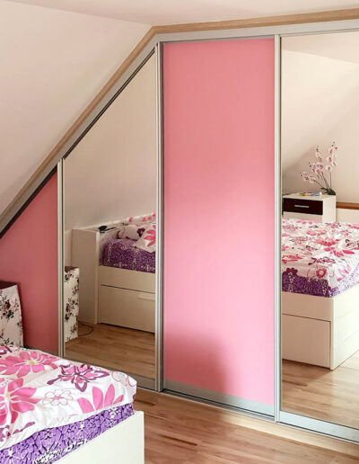 Realizace vestavěné skříně do ložnice v podkroví se zrcadlovými a růžovými dveřmi.