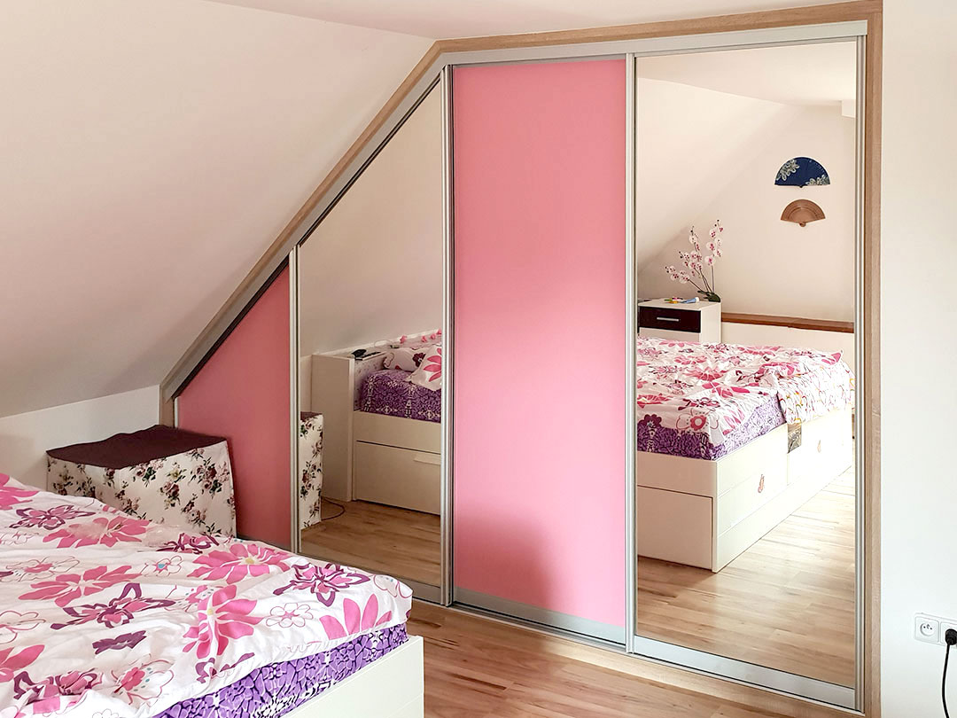 Realizace vestavěné skříně do ložnice v podkroví se zrcadlovými a růžovými dveřmi.