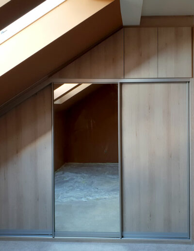Skříň na míru do ložnice v podkroví v dekoru dřeva s kombinovanými posuvnými a pantovými dveřmi.