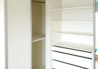 Interier rohové skříně na míru s posuvnými dveřmi v bílé barvě.