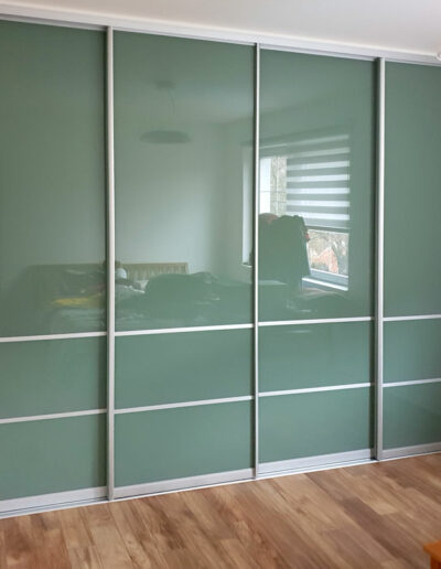 Realizace vestavěné skříně na míru s posuvnými dveřmi v hliníkovím rámu. Jako výplň byl použit zelený lacobel.