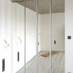 Realizace šatny uzavřené posuvnými zrcadlovými dveřmi ve stříbrném hliníkovém rámu.