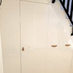Realizace vestavěné skříně s pantovými dveřmi do prostoru pod schody v bílé barvě.