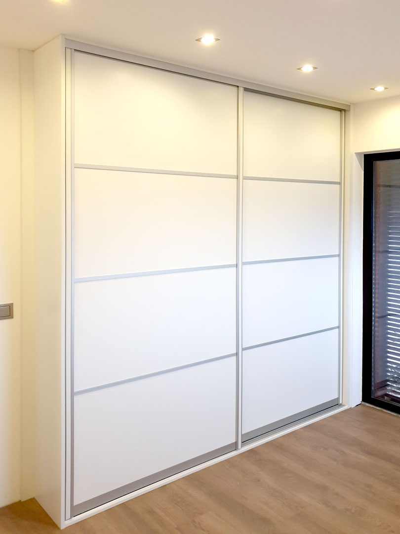 Realizace vestavěné skříně s posuvnými dveřmi s horizontálním dělením. Použity stříbrné hliníkové rámy a bílý dekor.
