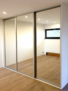 Realizace vestavěné skříně se zrcadlovými posuvnými dveřmi.