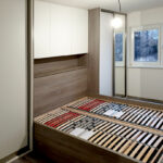 Ložnice na míru s postelí a vestavěými skříněmi v dekoru přírodní dub a krémová barva.
