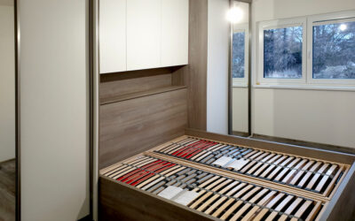 Ložnice na míru s postelí a vestavěými skříněmi v dekoru přírodní dub a krémová barva.